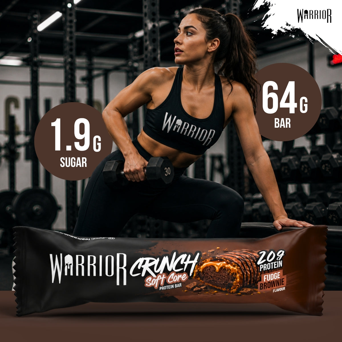 Warrior Crunch Soft Core Fudge Brownie protein bar wrapper on a gym floor, with a woman in Warrior kit holding a dumbbell behind it and callouts for 1.9g sugar and a 64g bar.